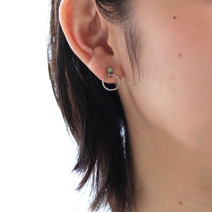 プラチナリングチャームとペリドットグリーンのピアスを耳に着けた女性の耳元画像