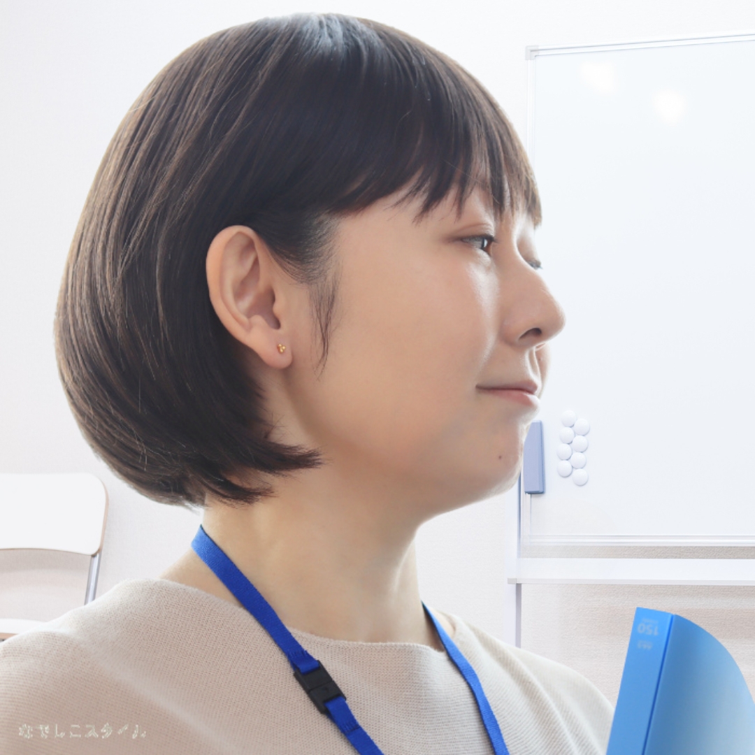 ゴールドカラーのキンモクセイの形の純チタンピアスをつけて仕事をしている女性の耳元画像
