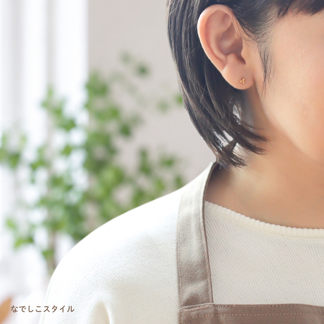 ゴールドカラーの金木犀の形の純チタンピアスをつけて家の中にいる女性

